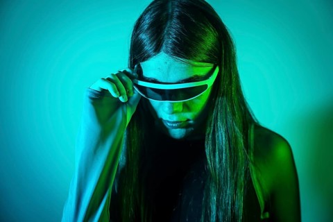 Futuristic studio portrait with neon lights of a non binary person with long hair using smart goggles