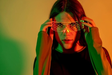 Futuristic studio portrait with neon lights of a transgender person looking at camera while using augmented reality goggles