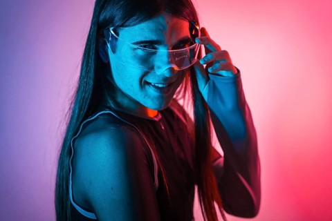 Futuristic studio portrait with neon lights of a cute non-binary person using smart goggles