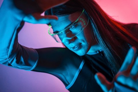 Futuristic studio portrait with neon lights of an androgynous person experimenting in the metaverse using augmented reality goggles
