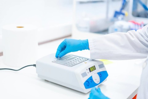Close-up photo of the hands of a biologist using a machine to work on cancer cells
