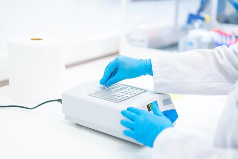 Hands of a biologist with protective blue latex gloves working on a machine to analyse cells