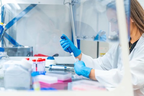 Woman working in a cancer research laboratory using a pipette to extract samples