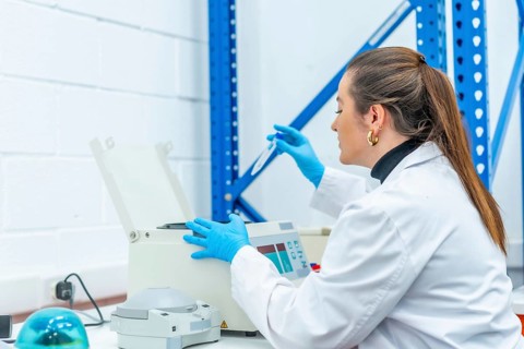 Female biologist extracting blood samples from a centrifuge machine sitting on a laboratory table