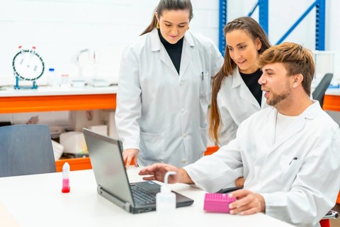 Doctor sitting on a table explain data to colleagues using laptop in a laboratory