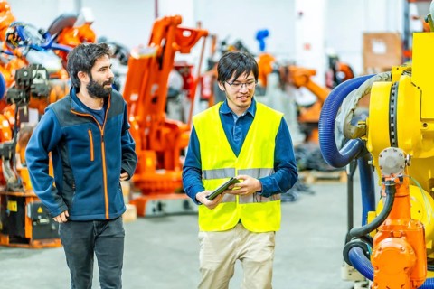 Team of engineers inspecting the machine in a robotic arm production line