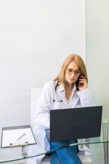 Female doctor talking on the phone to a patient while looking at her medical records on laptop in medical office