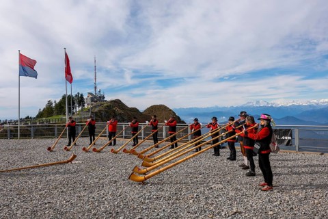 Group of Musicians Playing on Horns of the Alps with Mountainscape and View over Snow Capped Monte Rosa in a Sunny Day in Monte Generoso