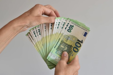 A hand counts many one hundred euro banknotes fanned out like in a card game