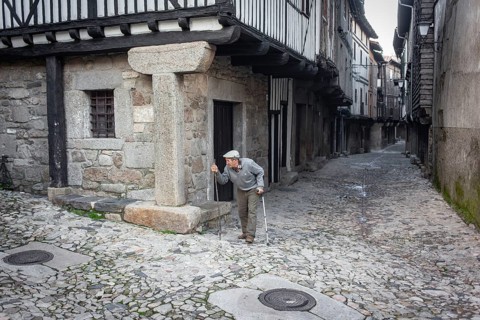 Old man with crutch and walking stick in an alley in La Alberca