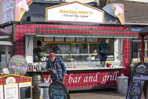 Old man in front of fish & chips and seafood stand in the city Oban
