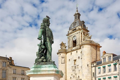 Statue of Victor Guy Duperre in front of the medieval clock tower in La Rochelle