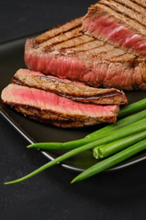 Closeup view of grilled tri-tip loin beef steaks medium rare with fresh vegetables on black background