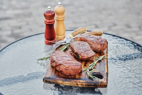 Tree juicy grilled strip steaks served on wooden cutting board
