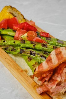 Grilled asparagus with bacon and corn on wooden serving board