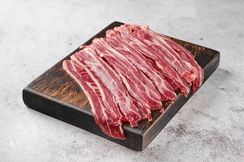 Fresh raw beef bacon strips on wooden cutting board