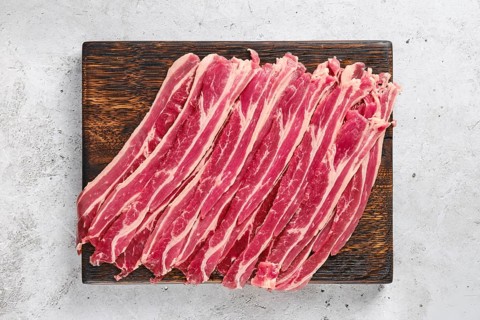 Top view of wooden cutting board with fresh raw beef bacon strips