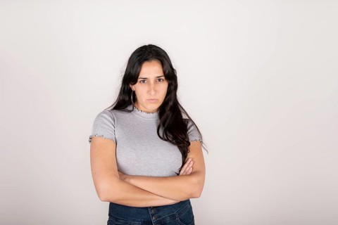 Portrait of a young latin woman dressed in a grey t-shirt with her arms crossed and an angry face