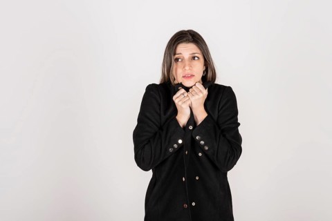 Studio portrait of young blonde woman wearing a black coat with expression of cold and disgust
