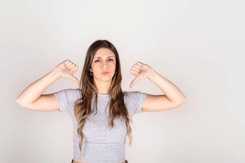 Blonde woman looking at camera with two thumbs down on white studio background. Concept of disapproval