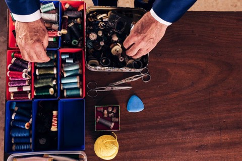 Overhead view male fashion designer s hand holding thread spool buttons from box wooden desk
