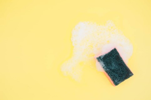 Overhead view sponge with soap sud yellow background