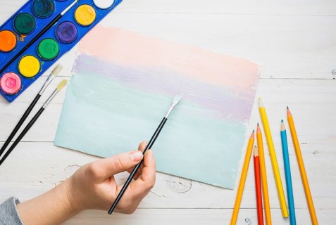 Person s hand painting paper with paint brush watercolor desk