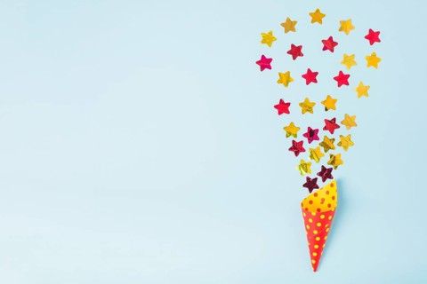 Star shape confetti coming out from paper cone with polka dot blue background