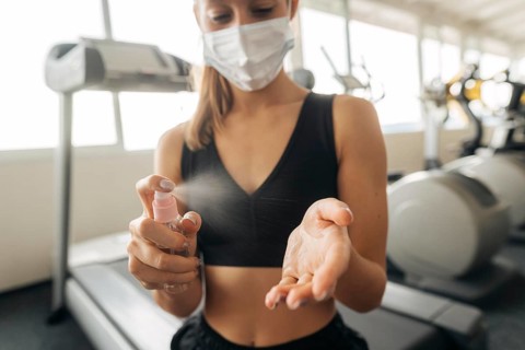Woman with medical mask gym using hand sanitizer