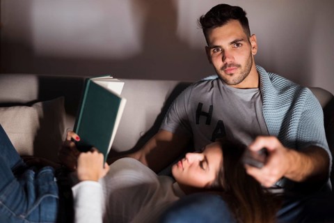 Young man with tv remote woman with book sofa