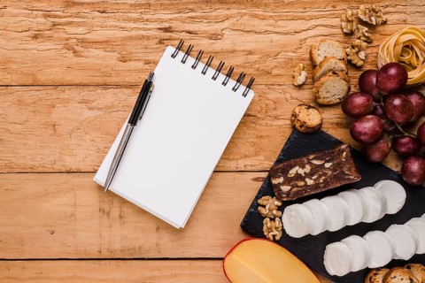 Blank spiral notepad with ballpoint pen near raw ingredients textured background