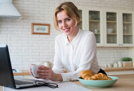 Cheerful business woman with coffee using laptop