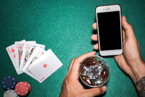 Close up hand holding cellphone whisky glass poker table