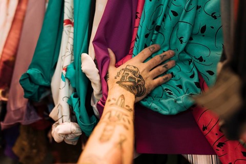 Close up man with tattoo his hand touching shirts arranged rail