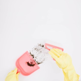 Close up yellow gloved hands sweeping dust into dustpan white background