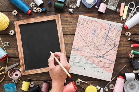 Crop hand drawing blackboard near sewing stuff