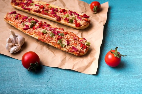 Delicious baguette pizza cherry tomato garlic brown paper blue concrete backdrop