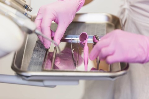 Dentist hand pink gloves arranging dental tools tray