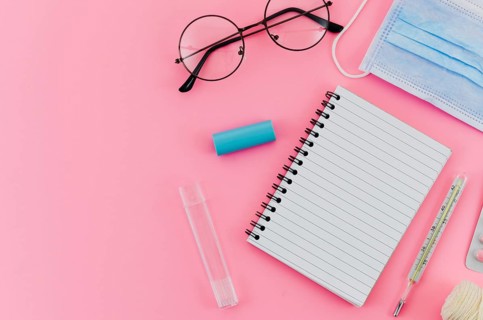 Eyeglasses thermometer surgical mask spiral notebook pink background