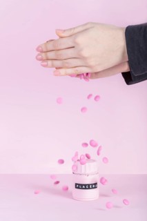 Female s hand falling pink pills placebo bottle pink background