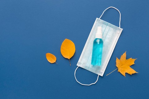 Flat lay medical mask with hand sanitizer autumn leaves
