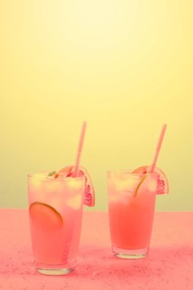 Fresh pink alcoholic cocktail with grapefruit lemon slice ice cubes against yellow background
