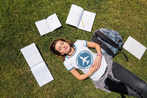 Girl lying grass surrounded by notebooks