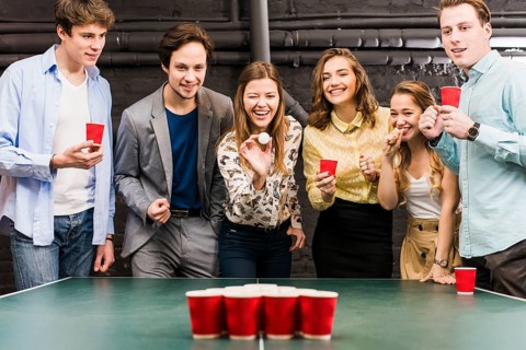 Group happy smiling friends enjoying beer pong game table bar