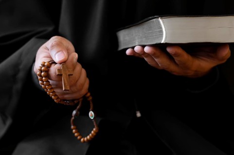 Person holding rosary with cross holy book
