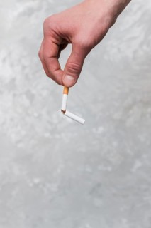 Persons hand holding broken cigarette old wall background