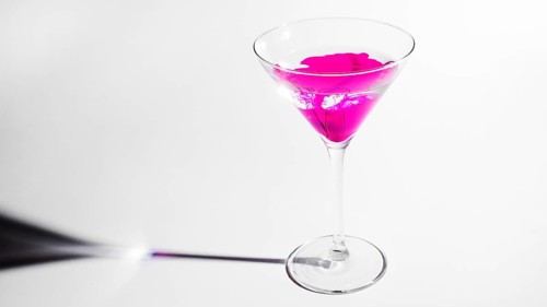 Pink ink dissolving martini glass isolated white backdrop