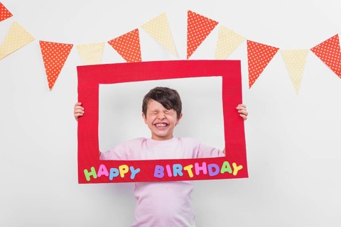 Portrait cute boy holding birthday frame with eyes closed