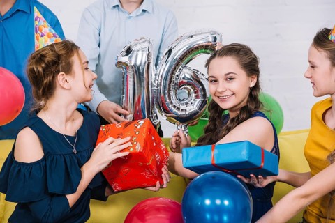 Smiling portrait birthday girl with number 16 foil balloon presents