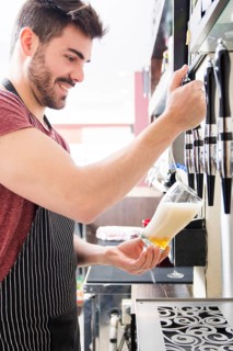 Smiling young male bartender pours fresh light beer from tap